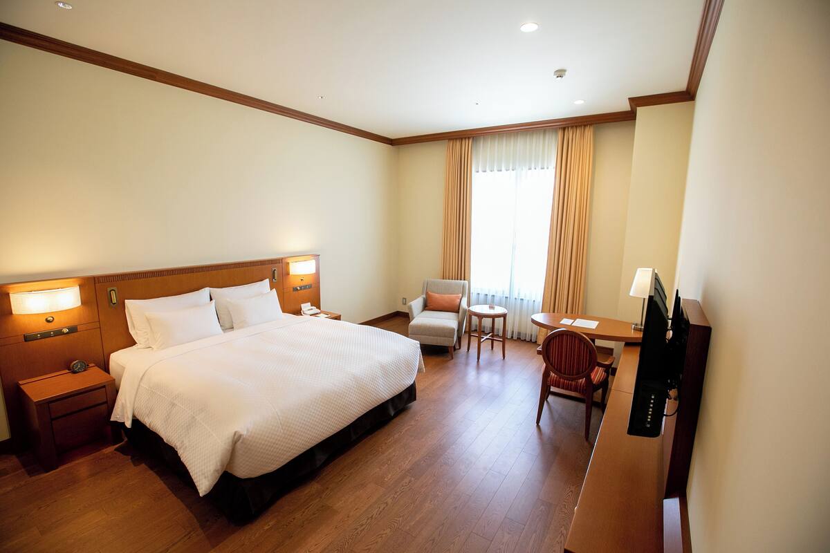 Een hotelkamer met een groot bed, een bureau met een computer, een stoel en een televisie.
