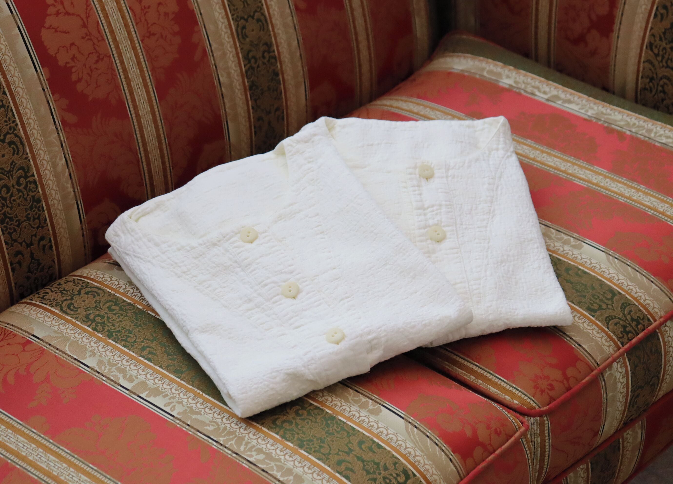Une couverture matelassée blanche, ornée de boutons, est posée sur un canapé à rayures et à motifs floraux.