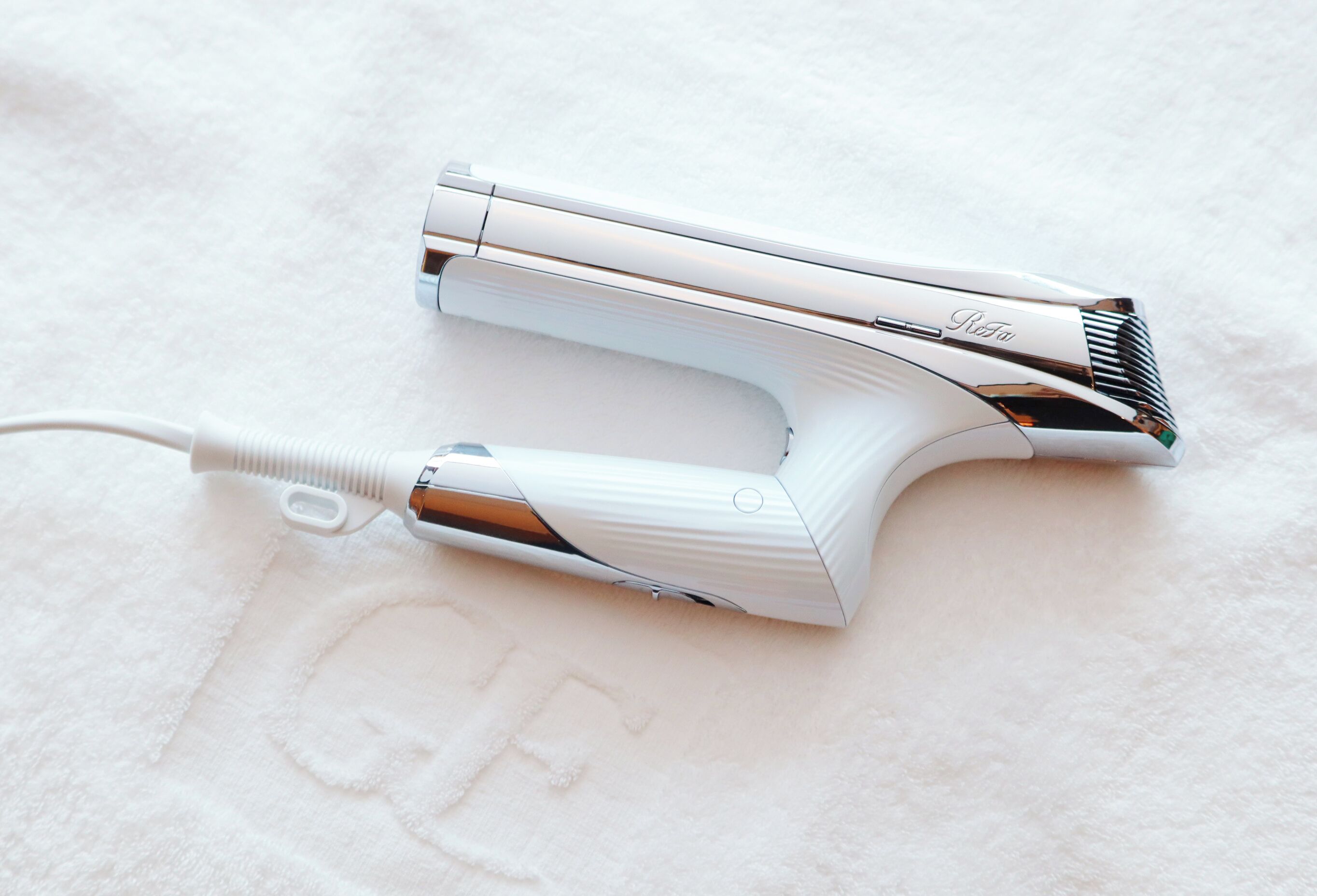 A white hair dryer with a cord on a white textured surface.
