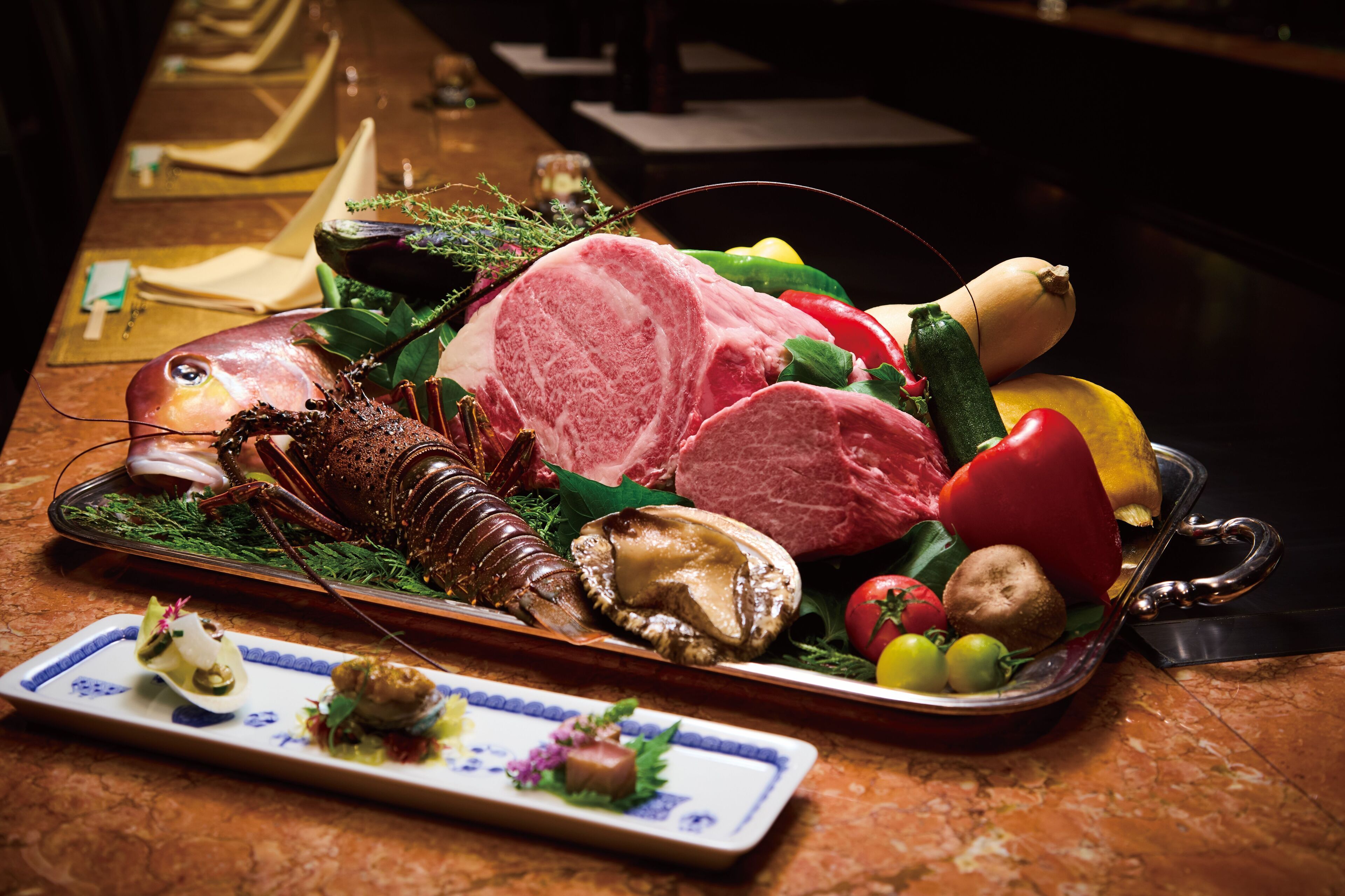 A seafood platter with various items including lobster, mussels, and shrimp, accompanied by vegetables and a small dish of appetizers.