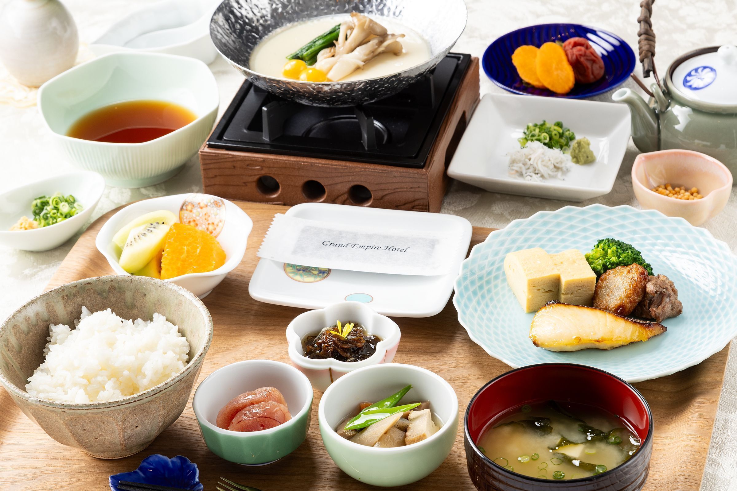 Forskellige japanske retter, herunder ris, suppe og kød, anrettet på et træbord.