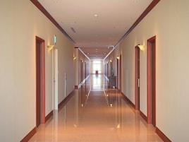 A long, well-lit hallway with doors on both sides, leading to a bright room at the end.
