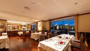 Un restaurant doté d’un plancher en bois, de tables dressées pour le dîner et de grandes fenêtres offrant une vue sur la ville la nuit.
