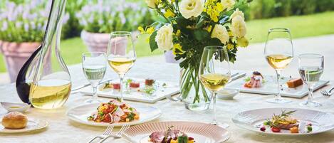 A table set for a meal with plates of food, glasses of white wine, and a vase of flowers.