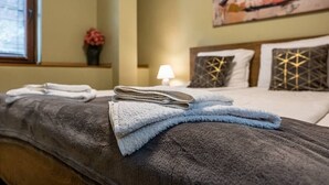 A neatly made bed with a grey blanket and folded towels, a bedside lamp, and a painting on the wall. - Karavelov Top Center Apartment (Varna)