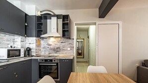 A modern kitchen with dark cabinets, a microwave, an oven, and a wooden dining table with chairs. - Karavelov Top Center Apartment (Varna)