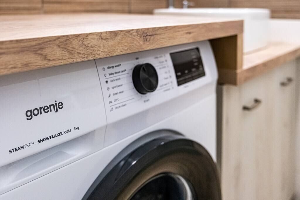 A front view of a white washing machine with a wooden countertop above it.