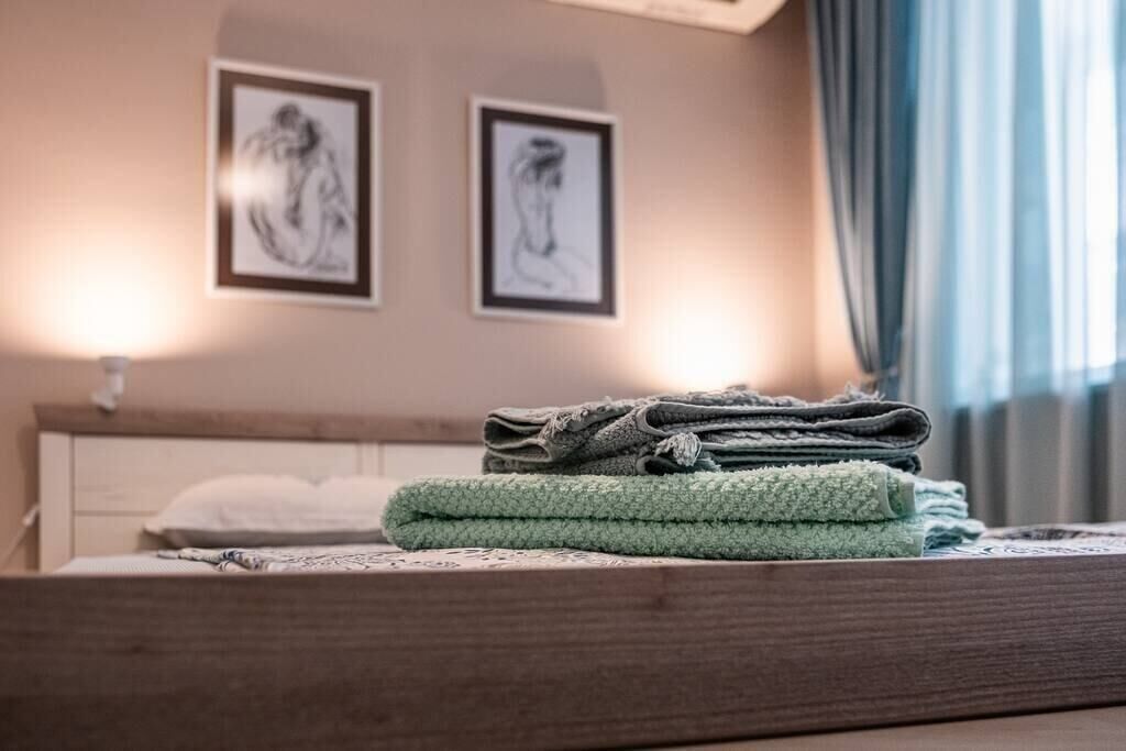 Un lit bien fait, avec une serviette verte, un oreiller blanc et une couverture à motifs. Deux œuvres d’art encadrées sont accrochées au mur, au-dessus du lit.