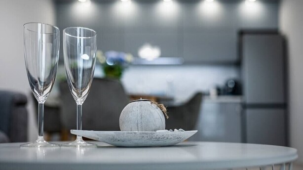 A modern kitchen with a round table in the foreground, two clear glasses, and a decorative stone on the table. - Brand New Downtown Apartment (Varna)