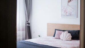 A bedroom with a bed, a headboard, a window with curtains, and a wall-mounted air conditioner. - Black Sea 2bdrm Central Apartment (Varna)