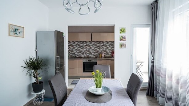 A modern dining area with a table set for two, a potted plant, and a decorative light fixture. - Black Sea 2bdrm Central Apartment (Varna)