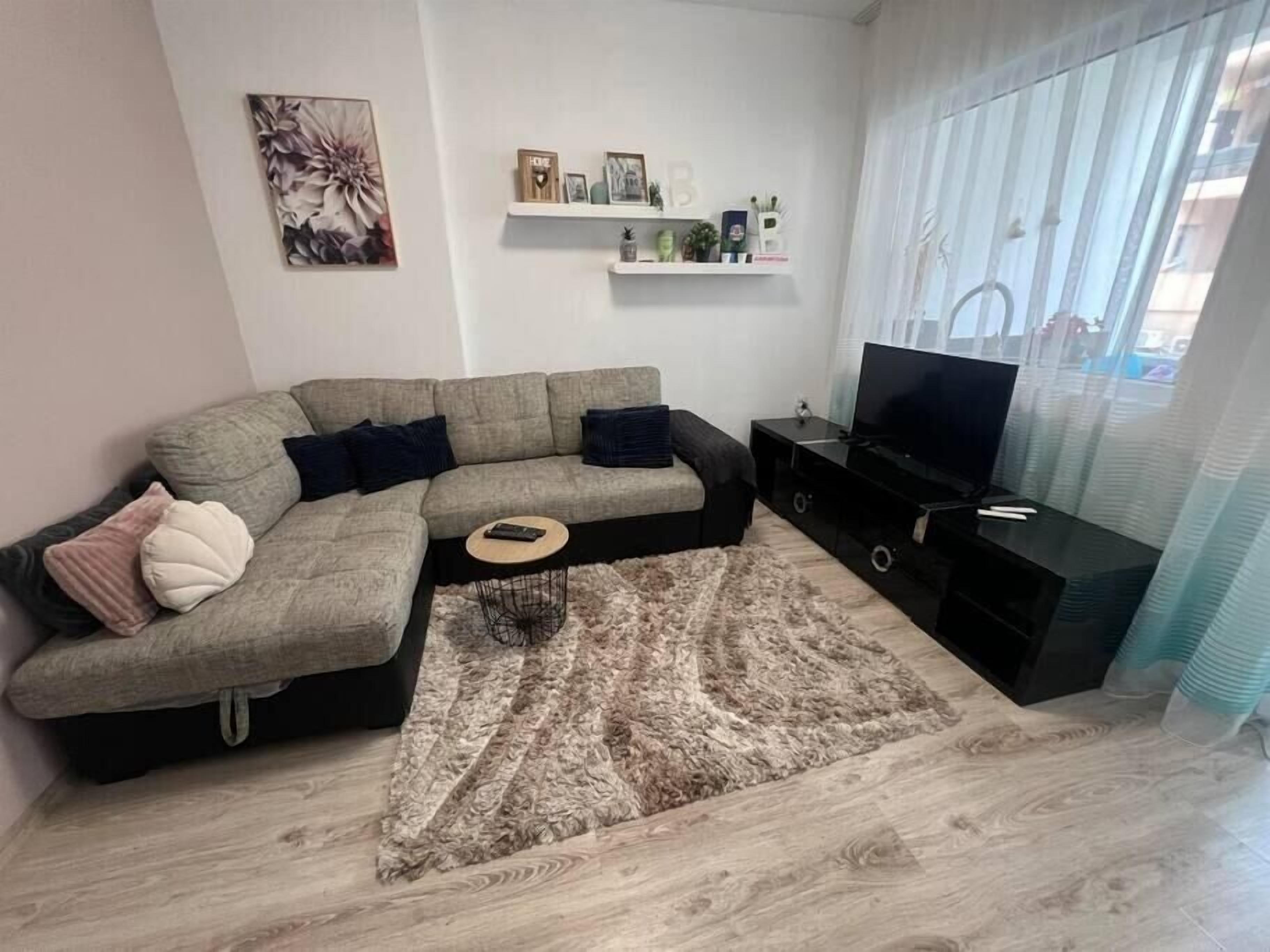 Uma sala de estar moderna com um sofá seccional, uma TV de tela plana e um tapete decorativo.