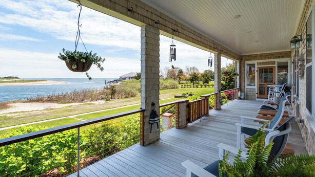 A covered outdoor deck with a view of the ocean, a grassy area, and a building in the background. - Charming 6-bedroom oceanfront cottage in Falmouth (Falmouth)