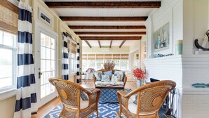 A room with a wooden floor, a blue patterned rug, wicker chairs, a sofa with patterned cushions, and a white brick fireplace. - Charming 6-bedroom oceanfront cottage in Falmouth (Falmouth)