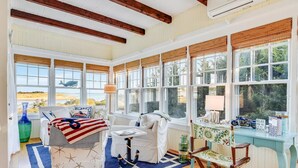 A sunlit room with a large window, a white sofa, a small table, and a chair. - Charming 6-bedroom oceanfront cottage in Falmouth (Falmouth)