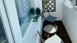 Un pequeño balcón con una silla blanca, una mesita y un panel decorativo con plantas.