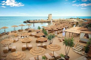 A beachside resort with numerous sun loungers and thatched umbrellas, a castle-like structure in the background, and a clear view of the sea. - Seaside Luxury Complex Apartment (Varna)