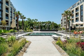 A modern outdoor pool area with a clear view of the pool, surrounded by palm trees and greenery. - Seaside Luxury Complex Apartment (Varna)