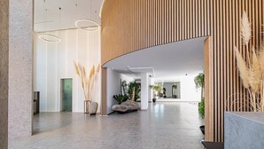 Een ruime lobby met een gebogen houten wand, een stenen bank en een receptiebalie.