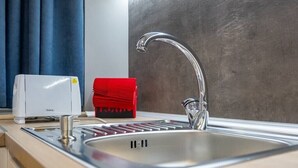 Une cuisine moderne avec un évier en acier inoxydable, un appareil électroménager rouge et un appareil blanc posé sur le plan de travail.