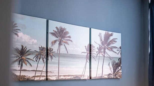 Un mur orné d’une grande œuvre d’art composée de trois panneaux, représentant des palmiers et une scène de plage.