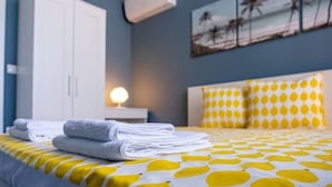 Un lit bien fait, recouvert d’une couverture à pois jaunes et blancs, avec un oreiller blanc à pois jaunes et une serviette blanche pliée posée sur le lit.