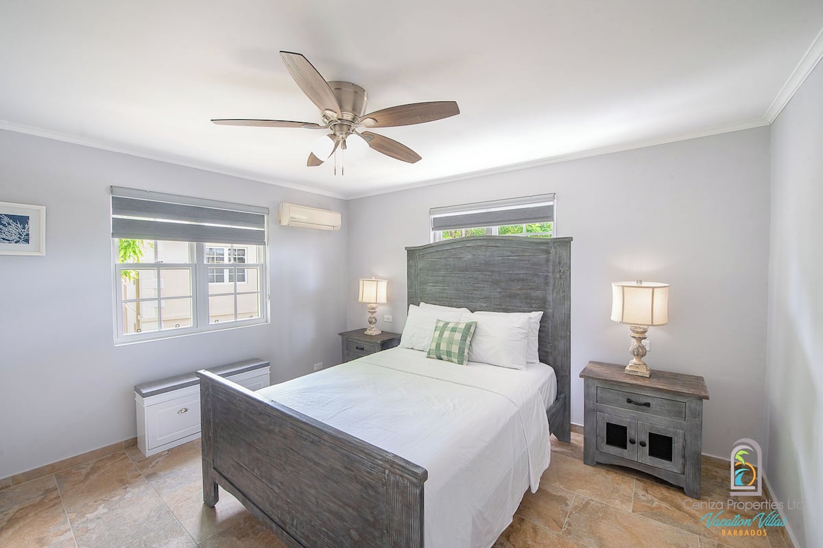 A bedroom with a bed, a ceiling fan, bedside tables with lamps, a window, and a radiator.