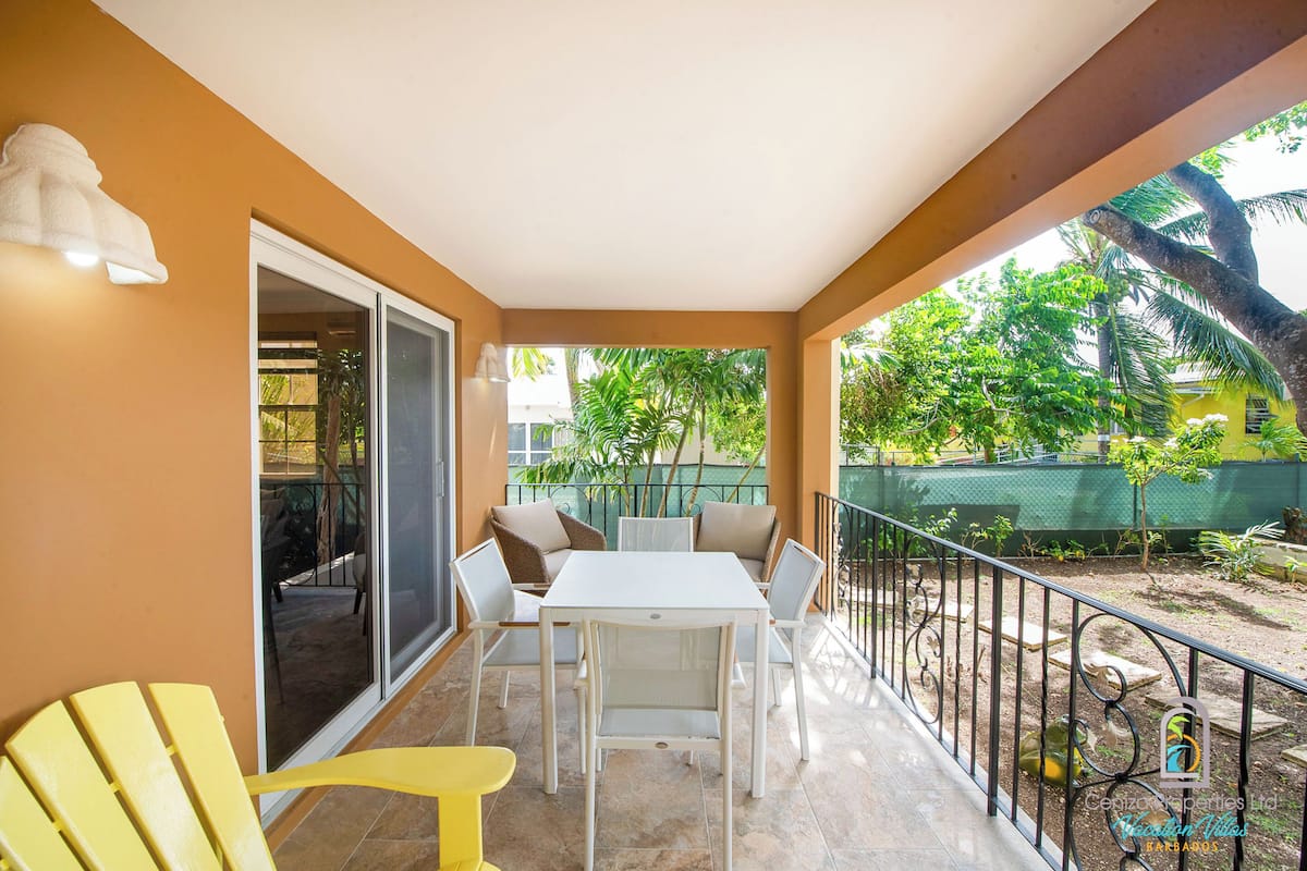 A balcony with a white table and chairs, a yellow chair, and a glass door leading to an indoor area.