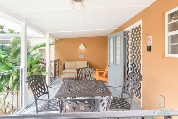A covered outdoor patio with a table and chairs, a sofa, and a door with a security gate.