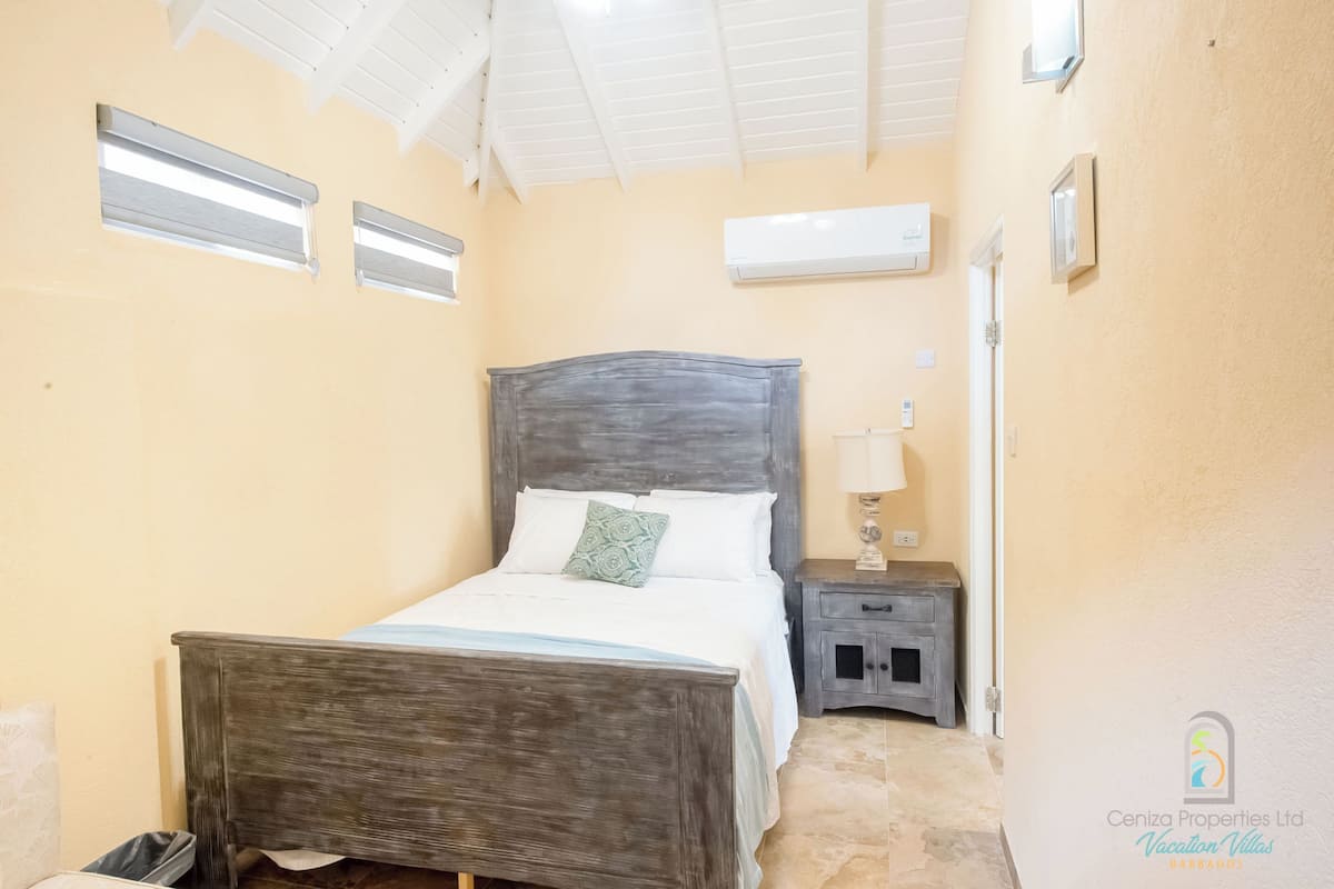A bedroom with a wooden bed, a nightstand, a lamp, and an air conditioning unit.