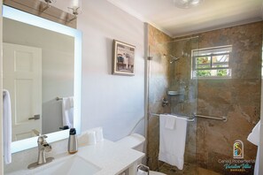Ein Badezimmer mit einer Duschkabine, einem weißen Waschbecken, einem großen Spiegel und einem gerahmten Bild an der Wand.