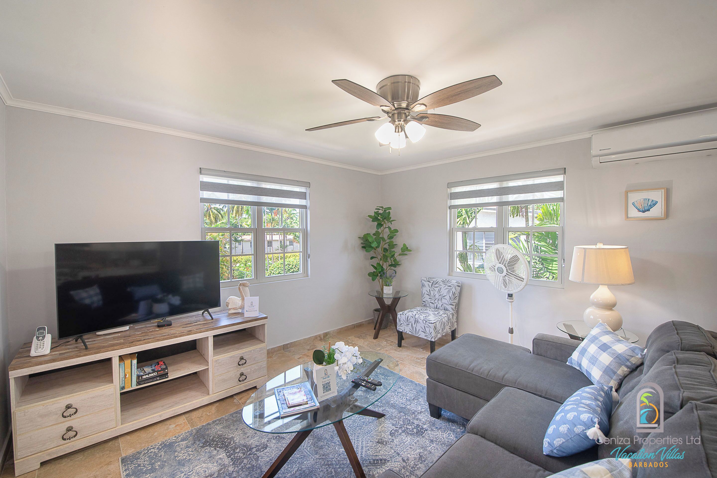 Ein Wohnzimmer mit Flachbildfernseher, Deckenventilator, einer Couch, einem Couchtisch und einem Sessel.