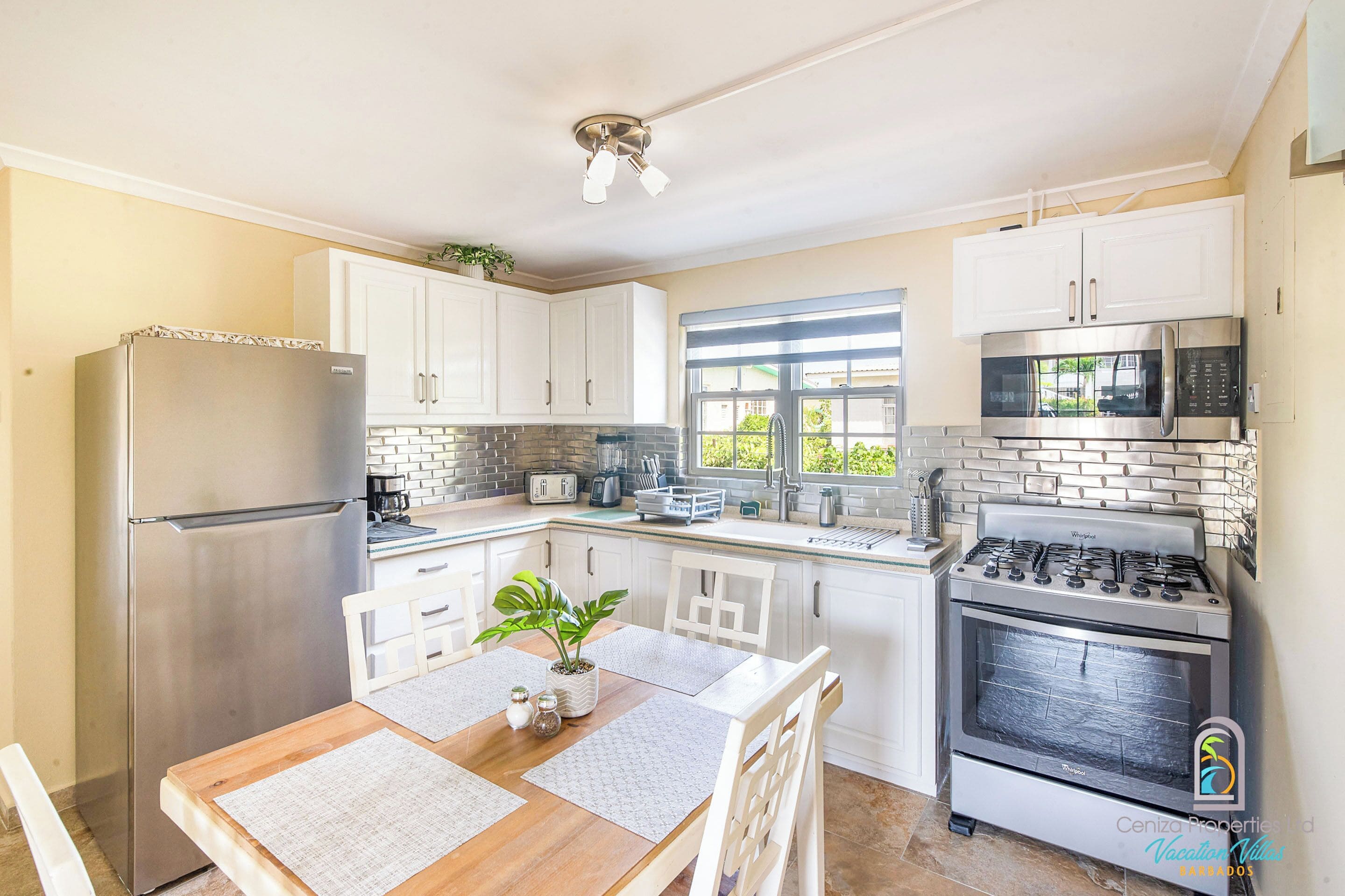 A modern kitchen with white cabinets, a stainless steel refrigerator, a microwave, a stove, and a dining table with chairs.