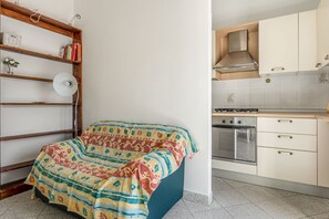 A bedroom with a bed, a wooden bookshelf, and a kitchen with cabinets and a stove.