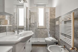 Une salle de bain moderne dotée d’une douche à parois de verre, d’un meuble-lavabo à deux vasques, de toilettes et d’un bidet.