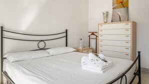 Un lit bien fait, avec du linge de lit blanc, une table de chevet en bois sur laquelle se trouve une lampe, une commode avec des tiroirs et un tableau encadré accroché au mur.