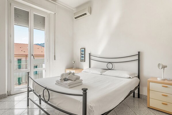 Un dormitorio con cama, mesita de noche, lámpara y vistas al exterior.