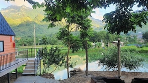 A wooden house with a blue roof, a balcony, and a view of a lake and mountains. - Milk Homestay  (Du Gia)