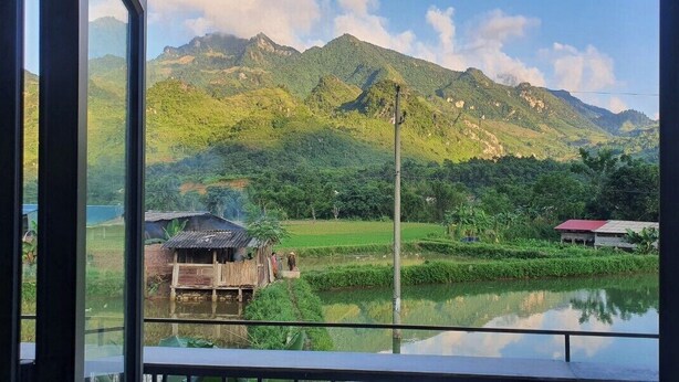 A view from a window of a rural landscape with mountains, a pond, and traditional houses. - Milk Homestay  (Du Gia)