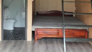 A compact room with a loft bed, a small bathroom, and a wooden floor. - Milk Homestay  (Du Gia)