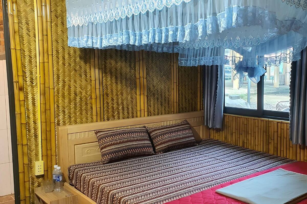 Une chambre à coucher avec un lit, une tête de lit en bois, une couvre-lit rouge et une fenêtre avec des rideaux.