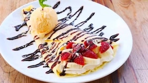 A dessert plate with banana slices, strawberries, and a scoop of ice cream, drizzled with chocolate sauce. - Milk Homestay  (Du Gia)