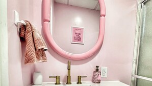 A bathroom with a pink vanity, two sinks, a mirror, and a towel rack. - The Dollhouse  (Old Orchard Beach)