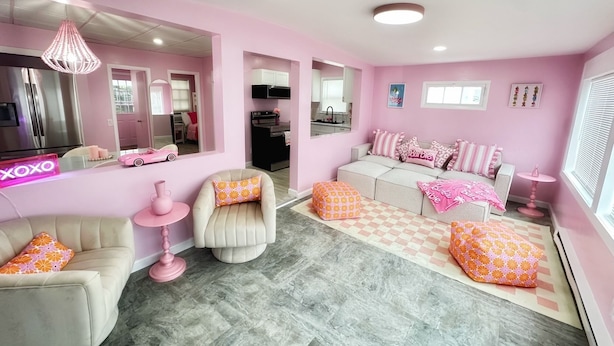 A pink-themed living room with a sofa, armchairs, ottomans, and a pink neon sign. - The Dollhouse  (Old Orchard Beach)