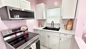 A modern kitchen with stainless steel appliances, a black oven, white cabinets, and a marble countertop. - The Dollhouse  (Old Orchard Beach)
