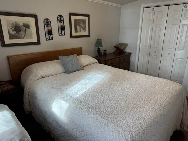 Un lit bien fait, recouvert d’une couvre-lit à motifs, une table de chevet avec une lampe et une armoire à plusieurs portes.