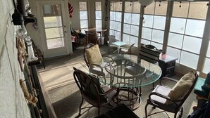 Una habitación soleada con una mesa de vidrio rodeada de sillas de mimbre, un ventilador de techo y ventanas amplias.