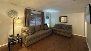 Ein Wohnzimmer mit zwei Sofas, einer Stehlampe, einer Uhr und einem Fenster mit Jalousien.