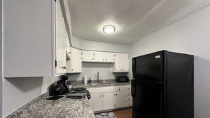 Eine kompakte Küche mit weißen Schränken, einem schwarzen Kühlschrank und einer Arbeitsplatte aus Granit.