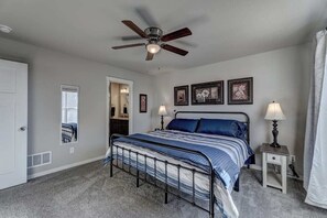 Una camera da letto con un letto, comodini, una ventola a soffitto e opere d'arte incorniciate al muro.